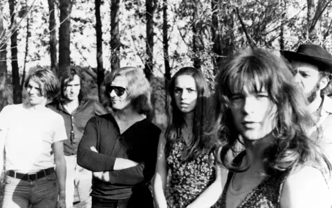Un groupe rock allemand des années 70, avec des membres aux cheveux longs et des tenues décontractées, posant devant des arbres.