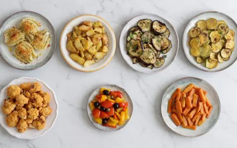 Sette piatti di verdure in friggitrice ad aria: finocchi, patate, melanzane, zucchine, cavolfiore, peperoni e carote.