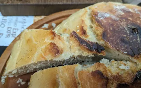 Ein knuspriges, goldbraunes dutch oven brot mit einer luftigen Krume, auf einem Holzbrett serviert.