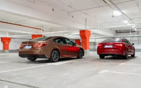Brązowa Toyota Camry i czerwona Skoda Superb stoją w garażu podziemnym.