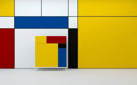 A cabinet in the style of De Stijl art, featuring primary colors and geometric shapes, stands against a wall with similar bold lines and blocks of yellow, red, blue, and white.