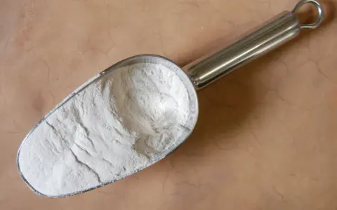Une pelle métallique remplie de poudre blanche, peut-être de la colle gomme arabique, sur un fond texturé.