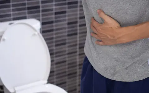 Mężczyzna trzyma się za brzuch, siedząc obok toalety. Może to być jeden z objawów raka odbytu.