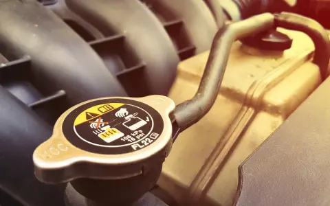 A car's radiator cap, showing warnings about hot coolant. A faulty cap can cause overheating, one of the bad radiator cap symptoms.
