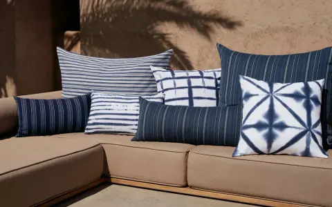 Idée déco plaid sur canapé : coussins bleus et blancs aux motifs rayés et tie-dye sur un canapé de jardin.