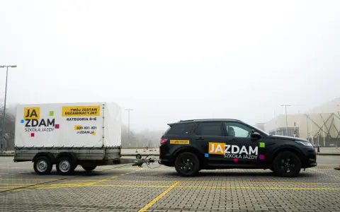 Czarny SUV z przyczepą szkoleniową "JA ZDAM" na placu manewrowym. Zestaw do kategorii B+E gotowy do egzaminu.