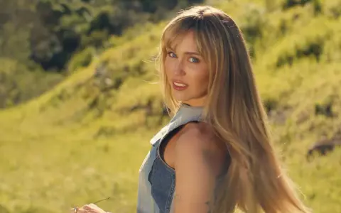 Miley Cyrus w nowej piosence, w letniej stylizacji, na tle zielonych wzgórz.