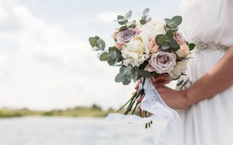 Un bouquet di rose e peonie, come quello che vorrei per a mia moglie, tenuto da una sposa con un abito bianco, con un lago sullo sfondo.