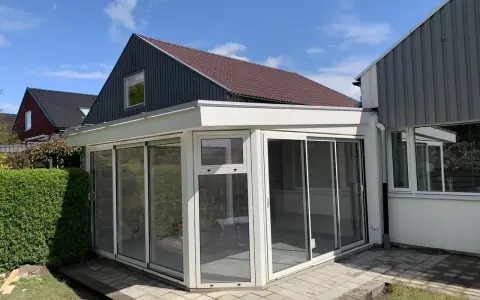 Ett modernt uterum med glaspartier och en vit takkonstruktion. Taklutningen på det angränsande huset ger en fin kontrast.