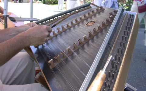 Dłonie grają na cymbałach, instrumencie strunowym, w słoneczny dzień.