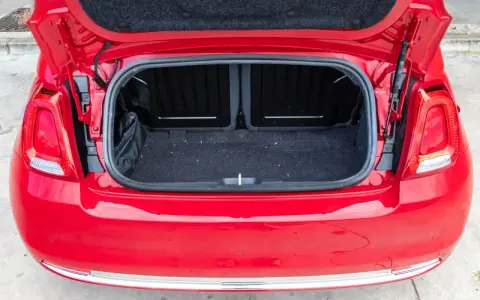Maletero abierto de un Fiat 500 rojo, mostrando el espacio de carga cubierto de fieltro oscuro.