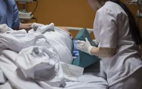 Asystent pielęgniarki, wykonując swoje uprawnienia, pomaga pacjentowi w łóżku, podkładając poduszkę.
