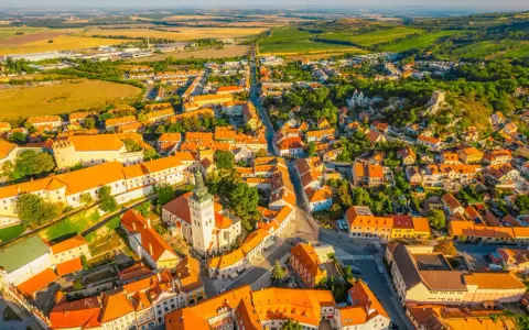 Malownicze miasteczko na Morawach w Czechach, z dominującą wieżą kościelną i pomarańczowymi dachami, otoczone zielonymi wzgórzami.