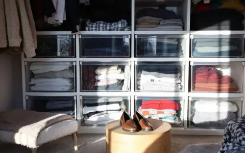 Des vêtements pliés dans des tiroirs transparents, une solution pour optimiser rangement vetements. Des chaussures marron sur une table basse.