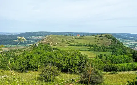 Grüne Hügel und Felder laden zum Walberla wandern ein. Ein kleiner Weg schlängelt sich zum Gipfel mit einem roten Haus.