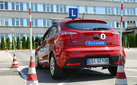 Czerwony samochód z literą "L" na dachu i napisem "EGZAMIN" na klapie. Na placu manewrowym, gdzie można sprawdzić, ile błędów można zrobić na egzaminie teoretycznym na prawo jazdy.