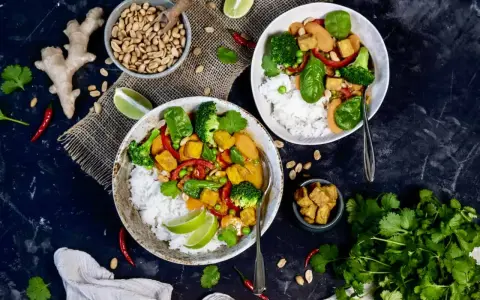 Zwei Schüsseln mit Reis, Tofu, Brokkoli und Erbsen. Ein Gericht, das vegan und proteinreich ist, mit Ingwer, Chili und Koriander garniert.