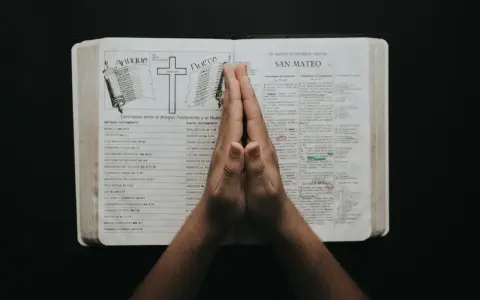 Dłonie złożone w modlitwie nad otwartą Biblią, z tekstami do modlitwy uwielbienia.