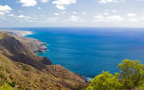 Blick auf die zerklüftete Küste und das tiefblaue Meer bei Cabo de Palos. Grüne Vegetation bedeckt die Hügel, die zum Meer abfallen.