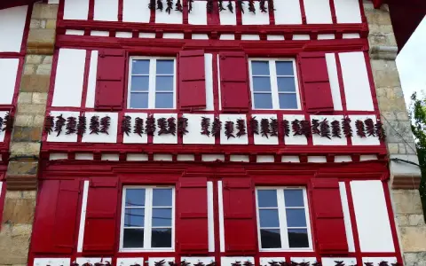 Façade rouge et blanche typique d'Espelette, avec des piments séchant. Combien de temps pour visiter Espelette ? Une journée suffit pour admirer ce village pittoresque.
