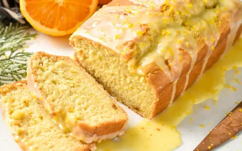 Un delicioso bizcocho de naranja, cubierto con glaseado y ralladura, con dos rebanadas cortadas.