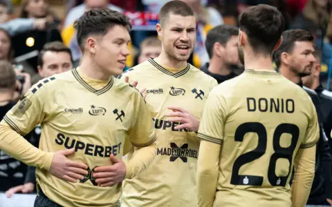 Piłkarze ręczni Górnika Zabrze w złotych strojach rozmawiają na boisku.