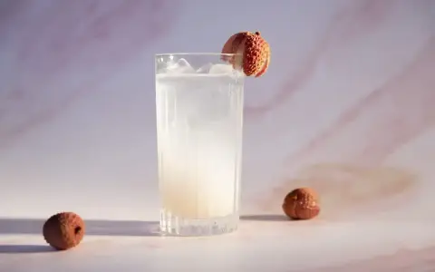 Orzeźwiający drink z liczi, ozdobiony owocem, z dwoma całymi liczi obok. Idealny na letnie popołudnie.