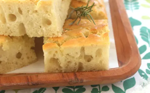 Focaccia alta e soffice, tagliata a cubetti, guarnita con rosmarino e sale grosso, servita su un tagliere di legno.