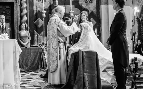 Sacerdote bendice a la pareja durante el rito de la velación. Novia con velo, novio de etiqueta, invitados y altar en iglesia.