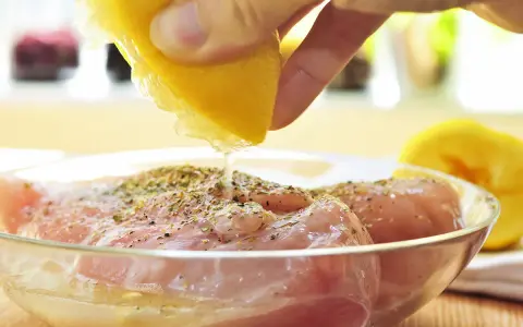 Préparation de la meilleure marinade poulet : un citron est pressé sur des morceaux de poulet assaisonnés dans un bol en verre.