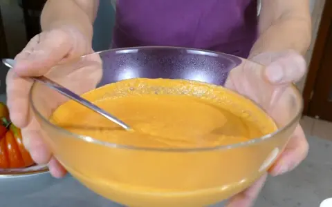 Mani che sorreggono una ciotola di vetro con una cremosa maionese di pomodoro, pronta per essere gustata.