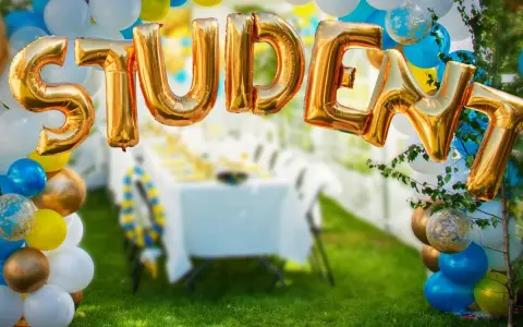 Gyllene folie ballonger bildar ordet "STUDENT" framför en festdukning utomhus.