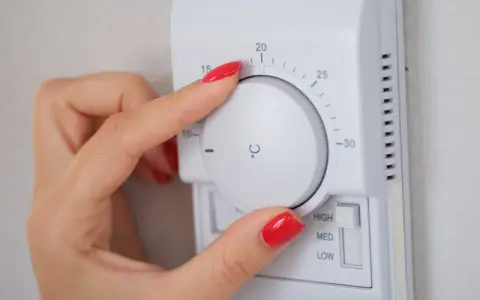 Dłoń z czerwonym lakierem reguluje termostat, ustawiając temperaturę dla elektro zaworów do CO.