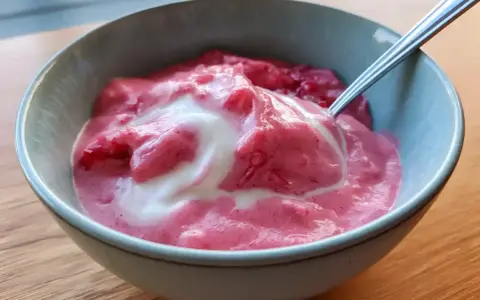 En skål med krämig rabarbercurd med en virvel av grädde. Perfekt för en somrig fika.