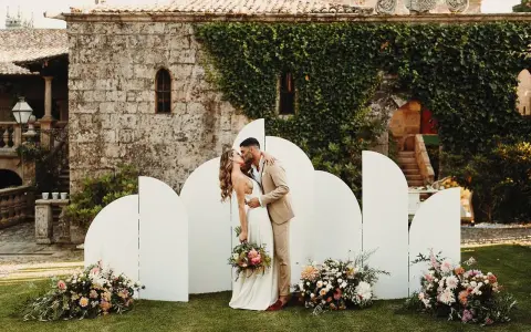 Novios besándose frente a un photocall moderno con arcos blancos y flores. ¡Ideas photocall boda únicas!