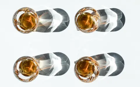 Vier Gläser mit bernsteinfarbenem Whiskey, die im Sonnenlicht stehen. Ein Vergleich zwischen Bourbon vs. Whiskey.