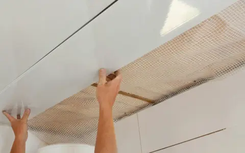 Mains installant des panneaux blancs pour refaire un plafond, avec un treillis visible en dessous.