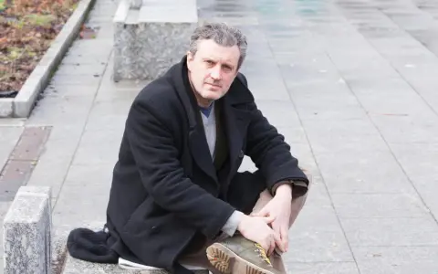 Uomo con cappotto nero seduto all'aperto, ricorda le atmosfere dei rocco schiavone libri.