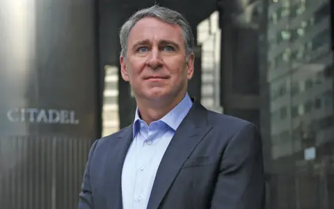 Ken Griffin, w eleganckim garniturze, stoi przed budynkiem z napisem "CITADEL".