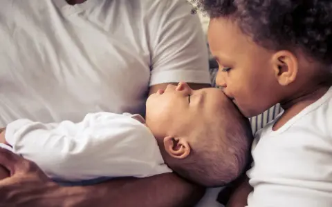 Ein älteres Kind küsst liebevoll die Stirn eines Babys. Die Frage "zweites Kind ja oder nein" scheint hier beantwortet.
