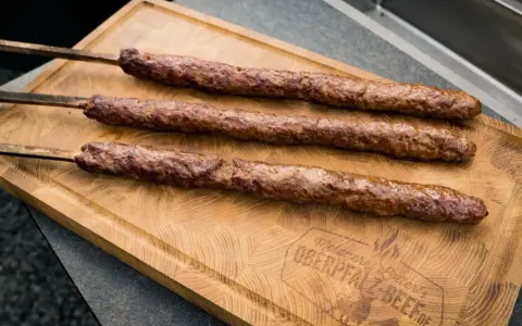 Drei saftige Adana Kebap Spieße liegen auf einem Holzbrett. Perfekt für ein authentisches Adana Kebap Rezept.