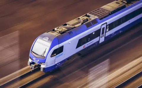 Pędzący pociąg TLK Flisak, którego rozkład jazdy jest kluczowy dla podróżnych, mija krajobraz w rozmytych barwach.