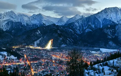 Oświetlone miasto Zakopane nocą, otoczone ośnieżonymi górami. Idealne miejsce na zakup biletów na zimowy wypoczynek.