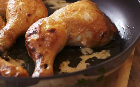 Cosce di pollo dorate e succulente cuociono in padella, emanando un profumo invitante.