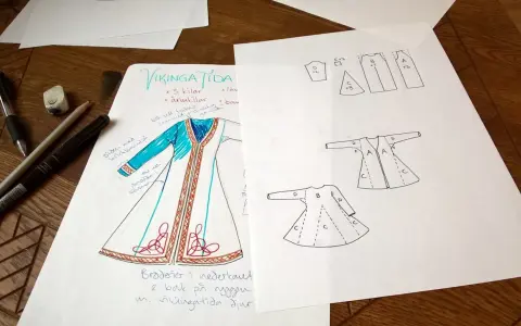 Skisser för en vikingatida kappa med mönster och sömnadsdetaljer. Pennor och suddgummi ligger bredvid.