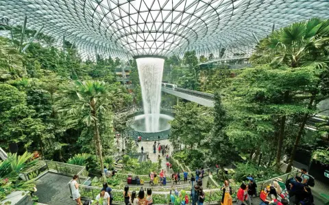 Imponerande vattenfall och frodig grönska under glastaket på singapore flygplats. Människor njuter av den unika miljön.