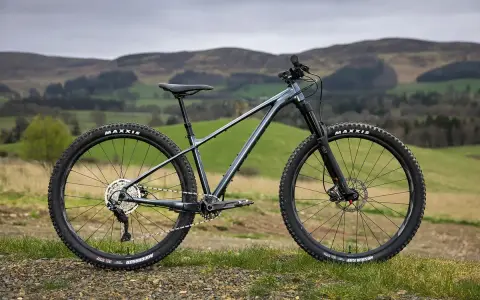A dark grey hard tail bike with knobby tires sits on a grassy hill, ready for adventure.