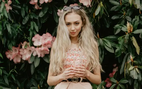 Blondynka w kwiecistej sukience, z okularami na głowie, otoczona różowymi kwiatami rododendronów. To kwintesencja słowiańskiej urody.