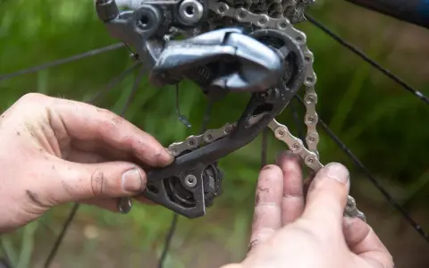 Smutsiga händer arbetar med att byta kedja på en cykel. Detaljbild på bakväxeln och kedjan.