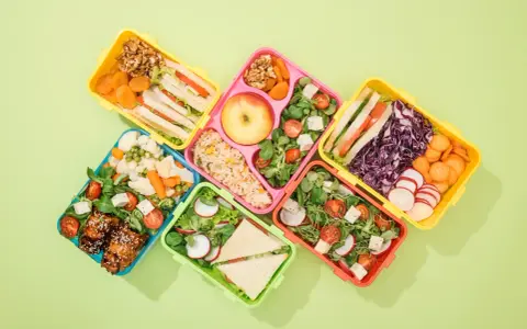 Kolorowe pojemniki na lunch z kanapkami, sałatkami, owocami i warzywami.
